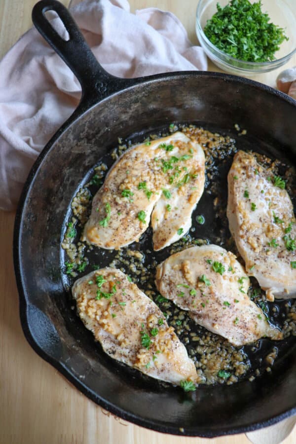 Cooked chicken breast covered in melted butter and garlic in a cast iron skillet.