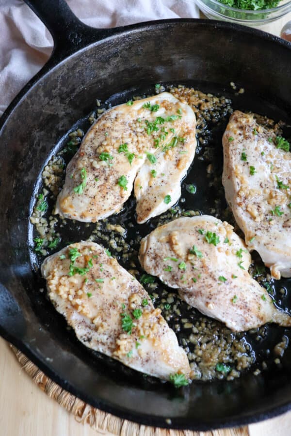 Cooked chicken breast covered in melted butter and garlic in a cast iron skillet.