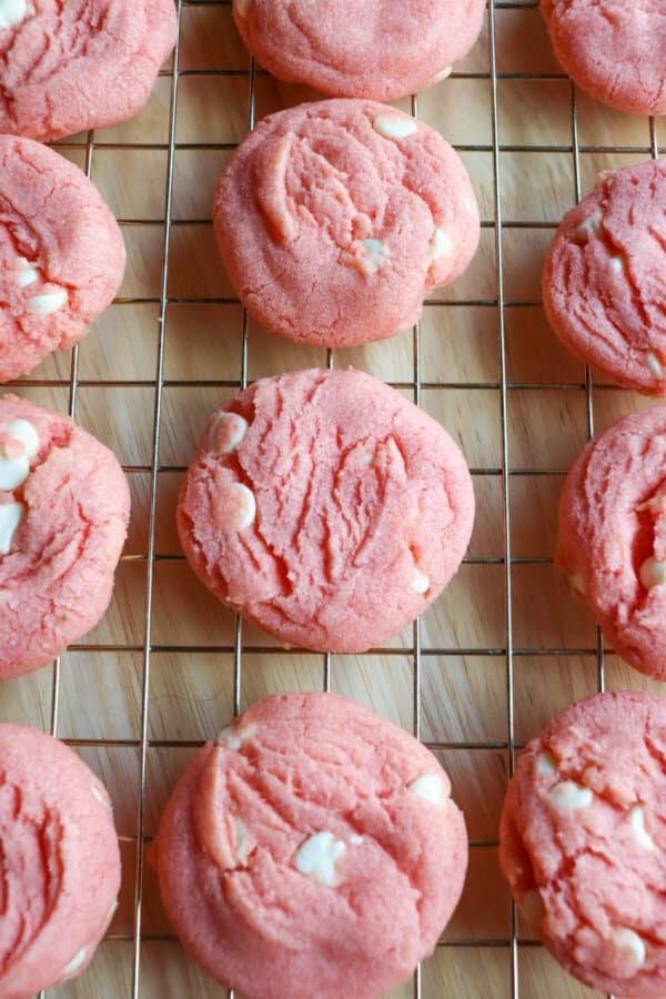 Pink cookies with white chocolate chips on a wire rack.