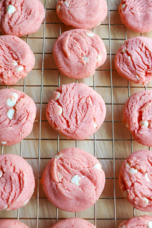 Pink cookies with white chocolate chips on a wire rack.