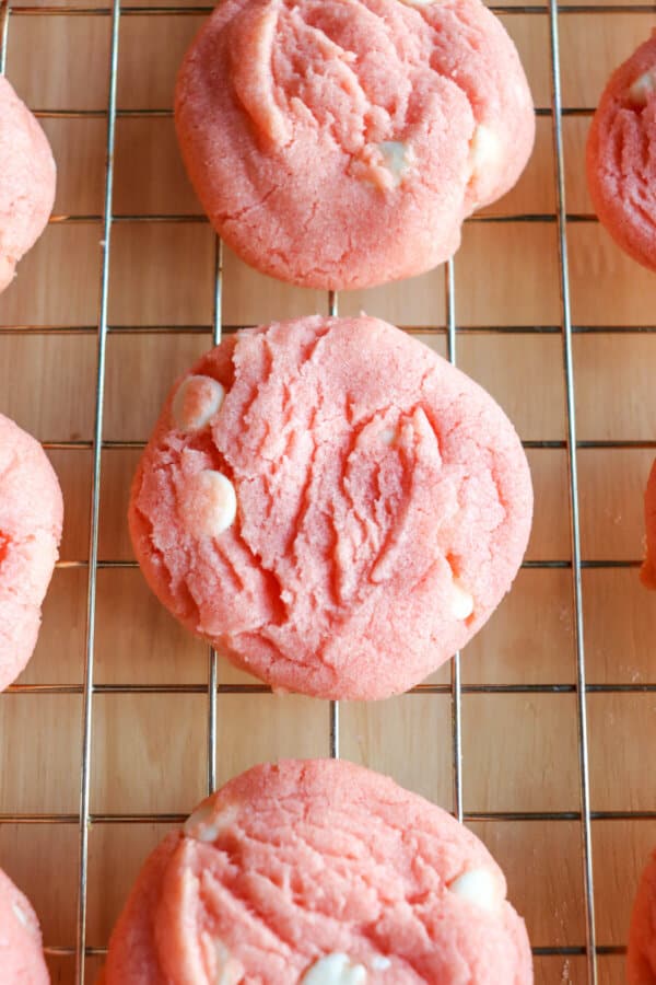 Close up of pink cookies with white chocolate chips on a wire rack.