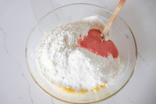 Flour, pudding mix and freeze dried strawberry powder in a clear glass bowl.