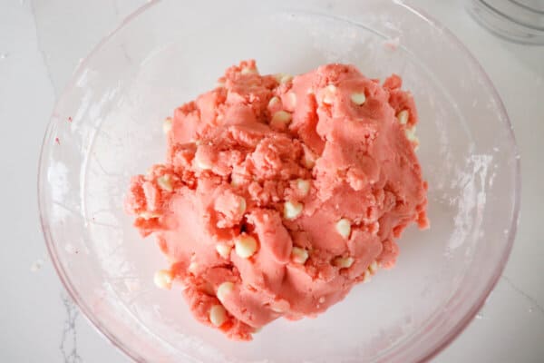 Pink cookie dough with white chocolate chips in a clear glass bowl.