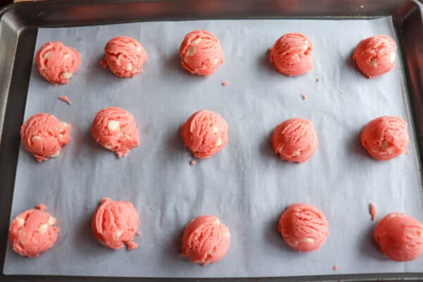 Pink cookie dough balls on a parchment paper lined baking sheet.