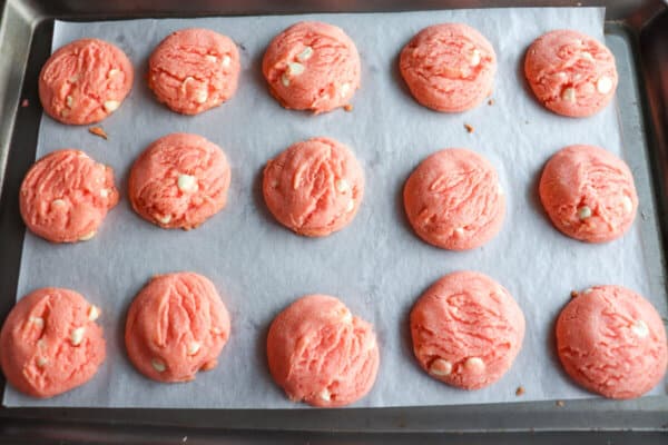 Pink cookies with white chocolate chips on a baking sheet.