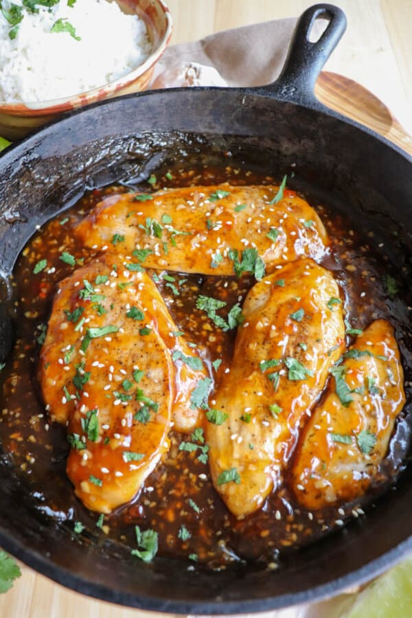Chicken breast covered in an orange sweet chili sauce topped with fresh cilantro and sesame seeds in a cast iron skillet.
