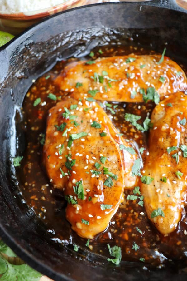 Chicken breast covered in an orange sweet chili sauce topped with fresh cilantro and sesame seeds in a cast iron skillet.