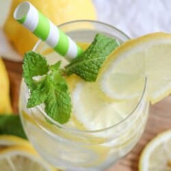 Glass of limoncello spritz with lemon slice garnish and mint leaves with a green and white straw.