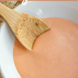 Spicy mayo sauce in a white bowl with a wooden spoon dipped in on the left.