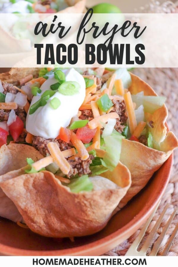 Taco salad topped with shredded cheese, green onion and sour cream in a tortilla bowl.
