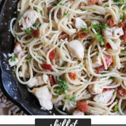 Cooked spaghetti in a cast iron skillet with chicken, bacon bits and garnished with fresh parsley.