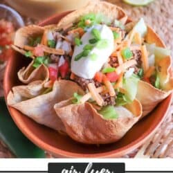 Taco salad topped with shredded cheese, green onion and sour cream in a tortilla bowl.