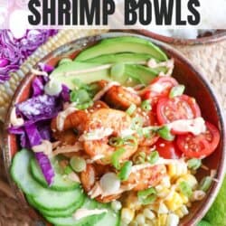 Cooked shrimp in a bowl surrounded by sliced cucumber, corn kernels, cherry tomatoes, sliced avocado and shredded red cabbage drizzled with spicy mayonnaise.