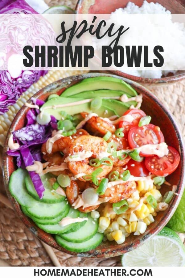 Cooked shrimp in a bowl surrounded by sliced cucumber, corn kernels, cherry tomatoes, sliced avocado and shredded red cabbage drizzled with spicy mayonnaise.