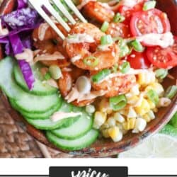 Cooked shrimp in a bowl surrounded by sliced cucumber, corn kernels, cherry tomatoes, sliced avocado and shredded red cabbage drizzled with spicy mayonnaise.