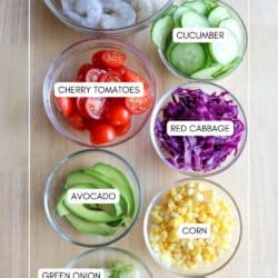 Ingredients for shrimp bowls in clear glass bowls on a wooden table.