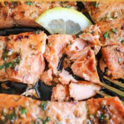 Salmon fillets in a cast iron skillet topped with fresh parsley and lemon slices.