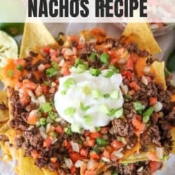Nachos piled high with ground beef, pico and melted cheese on parchment paper.