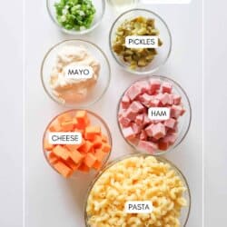 Ham & cheese pasta salad ingredients in clear glass bowls on a white counter.