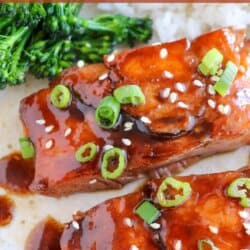 Salmon fillets covered in a rich brown sugar and bourbon glaze topped with green onions and sesame seeds on a white plate.