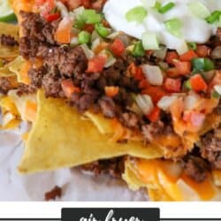 Nachos piled high with ground beef, pico and melted cheese on parchment paper.