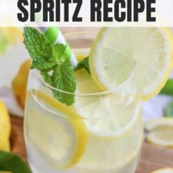 Glass of limoncello spritz with lemon slice garnish and mint leaves with a green and white straw.