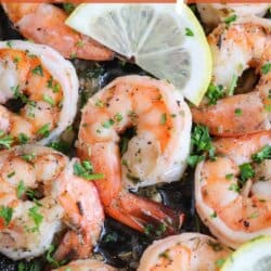 Cooked shrimp in garlic and butter on a cast iron skillet with fresh parsley and lemon slices for garnish.