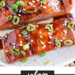 Salmon fillets covered in a brown sugar & bourbon glaze on a white plate with green onion and sesame seeds garnishing the fish.