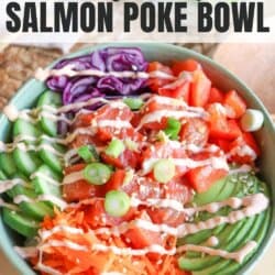 A green bowl with sliced cucumbers, grated carrot, sliced avocado, purple cabbage, diced red pepper with raw cubes of salmon topped with a drizzle of spicy mayo and diced green onion.