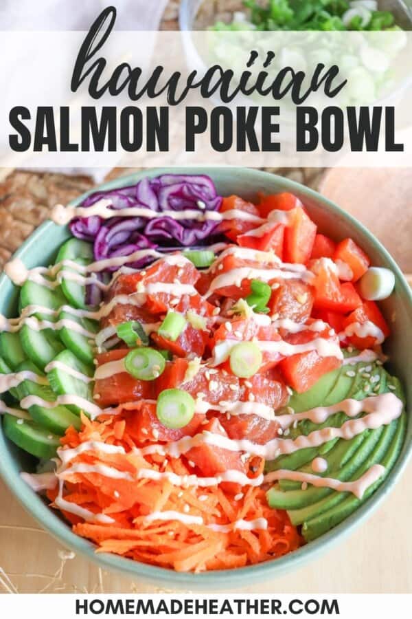 A green bowl with sliced cucumbers, grated carrot, sliced avocado, purple cabbage, diced red pepper with raw cubes of salmon topped with a drizzle of spicy mayo and diced green onion.