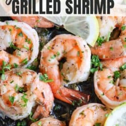 Cooked shrimp in a skillet topped with fresh parsley and lemon slices.