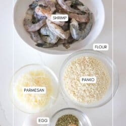 Ingredients for air fryer panko shrimp in clear glass bowls on a white counter.