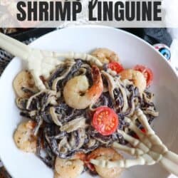 Purple and white linguine noodles in a cream sauce topped with shrimp and cherry tomatoes with skeleton hands in a white bowl.