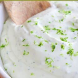 White bowl of crema sauce topped with lime zest with a wooden spoon dipped in on the left.
