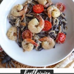 Purple and white linguine noodles in a cream sauce topped with shrimp and cherry tomatoes in a white bowl.