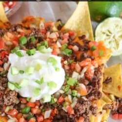 Nachos piled high with ground beef, pico and melted cheese on parchment paper.