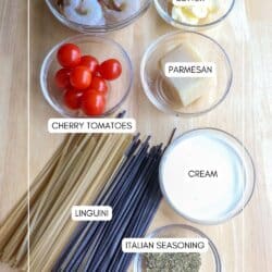Ingredients for shrimp linguini in clear glass bowls on a wood table.