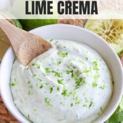 White bowl of crema sauce topped with lime zest with a wooden spoon dipped in on the left, surrounded by fresh lime and cilantro.