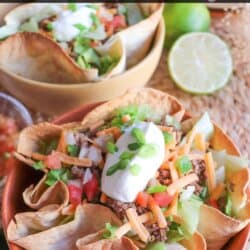 Taco salad topped with shredded cheese, green onion and sour cream in a tortilla bowl.
