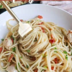 Cooked spaghetti in a cast iron skillet with chicken, bacon bits and garnished with fresh parsley.