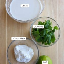 Ingredients for cilantro lime cream in clear class bowls on a wooden table.