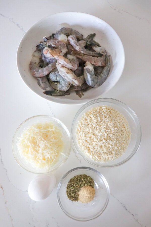 Ingredients for Panko shrimp in clear glass bowls on a white counter.