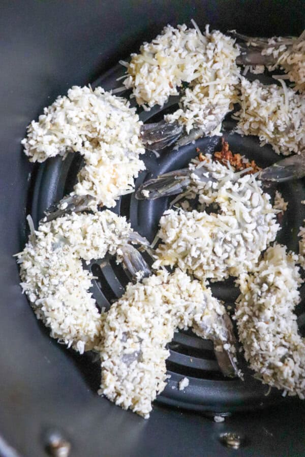 Raw Panko battered shrimp in the basket of an air fryer.