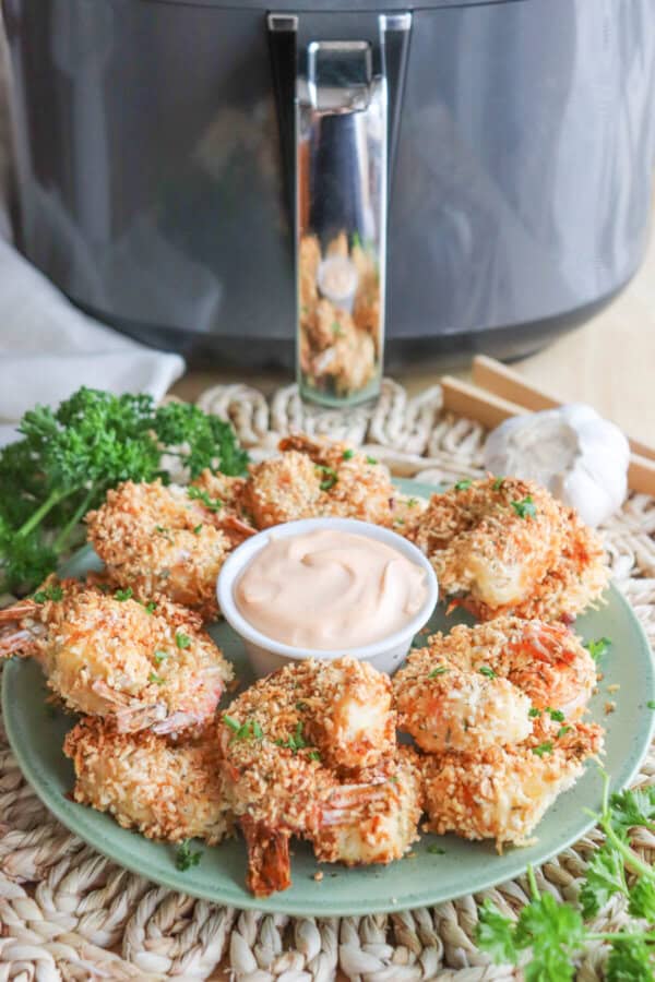 Air fried panko shrimp on a green plate surrounding spicy mayo with an air fryer in the background.