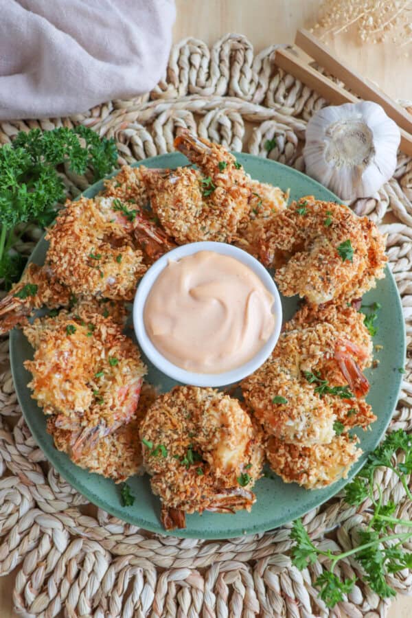 Air fried panko shrimp on a green plate surrounding spicy mayo with an air fryer in the background.