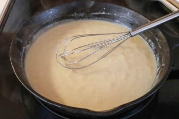 Cast iron skillet with creamy white rue with a whisk in it.
