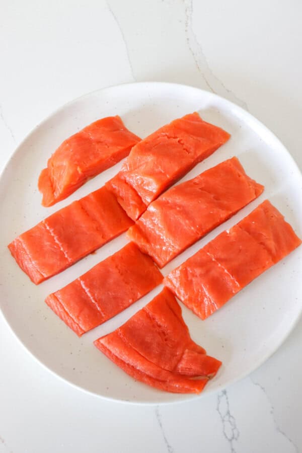 Salmon fillet prepared and cut into 2" strips on a white plate.