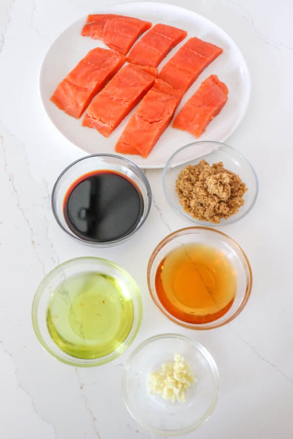 Salmon bourbon marinade ingredients in clear glass bowls on a white counter.