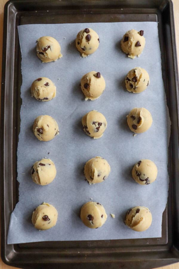Chocolate chip cookie dough balls on a parchment paper lined cookie sheet.