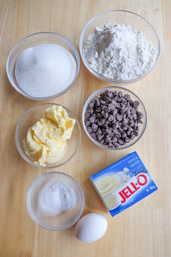 Ingredients for chocolate chip pudding cookies in clear glass bowls on a wooden table.